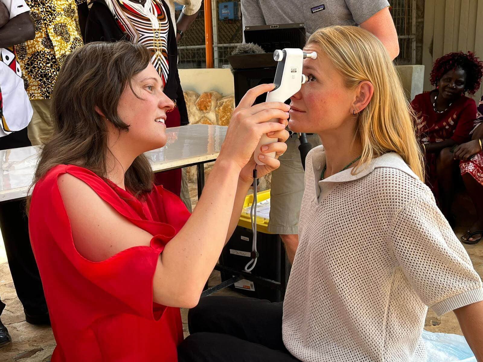 A woman with brown hair in a red top holds a device looking in the eye of a blonde woman in a white top