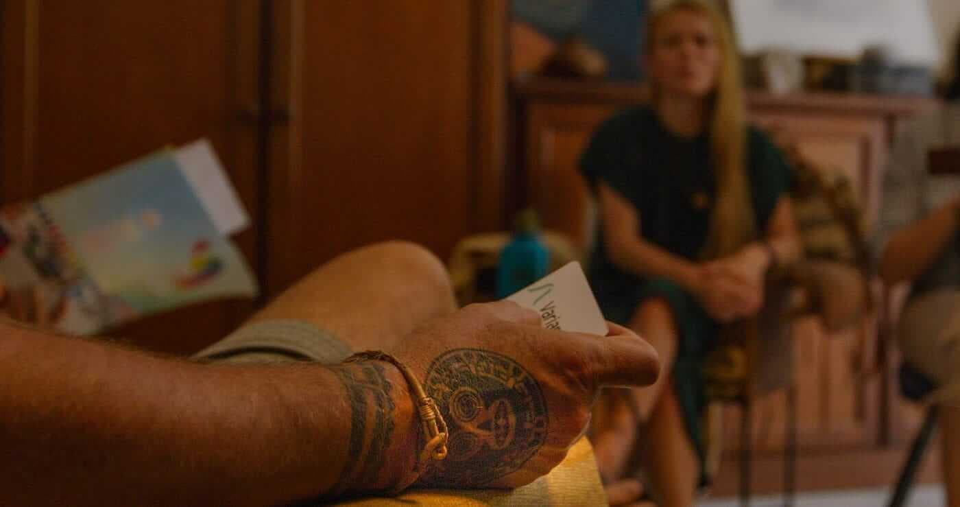 Closeup of a hand with a tattoo and a bracelet, holding a piece of paper that says Variant Bio. The outline of a woman in the background