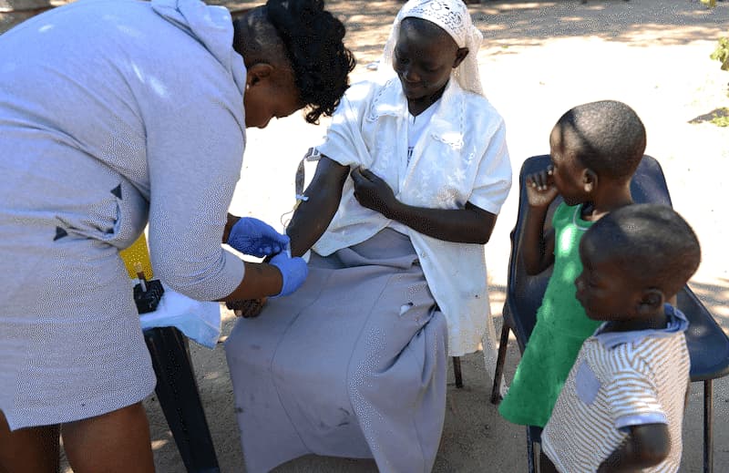 A woman giving a blood sample for testing with two children nearby