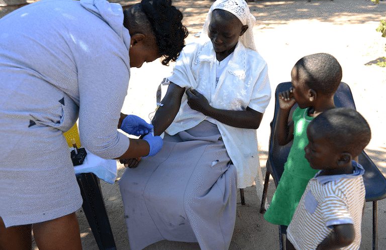 Community engagement in Limpopo, South Africa. Photo credit: Thabo Gumede A woman giving a blood sample for testing with two children nearby