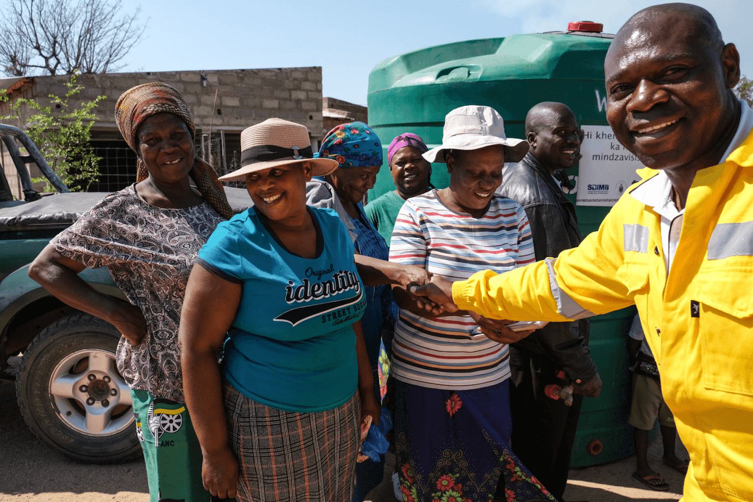 Seven people smiling, standing in front of a set of green water tanks